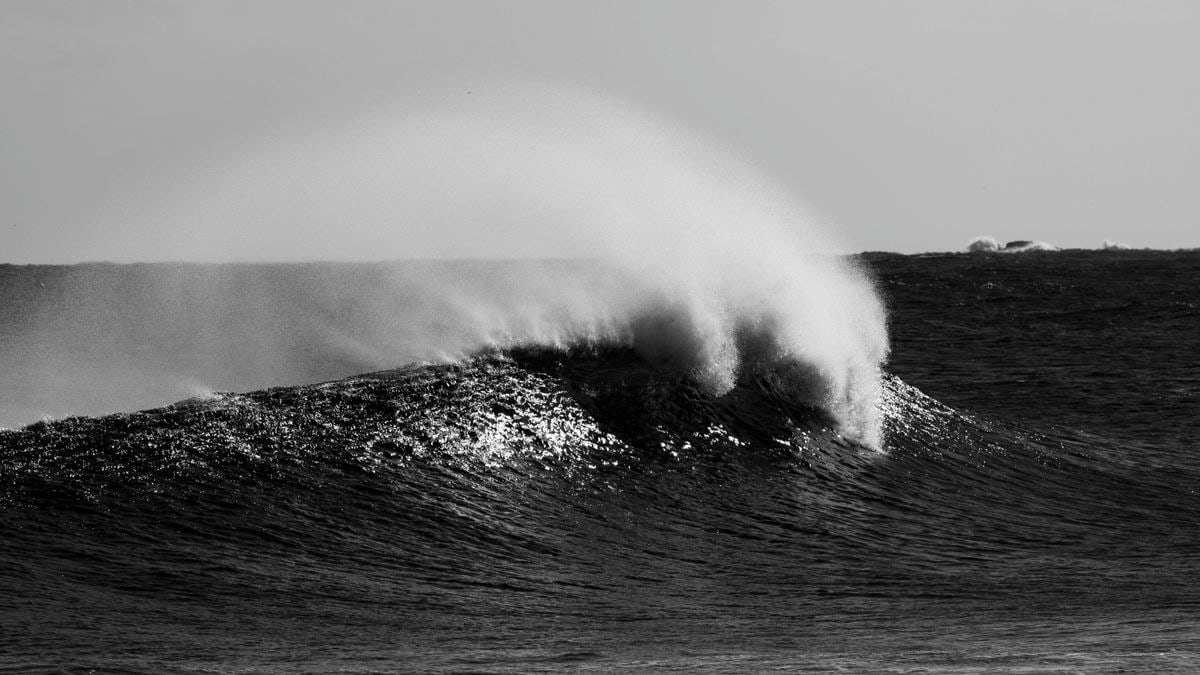 A dynamic black and white image of an ocean wave crashing with mist spray.